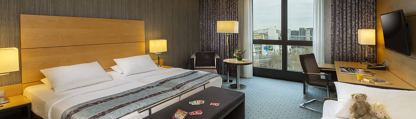 Chambre familiale Classic au Maritim Hotel Düsseldorf avec grand lit double, lit simple, cartes à jouer et peluches pour enfants.