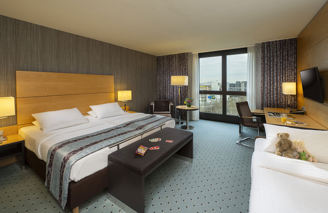 Chambre familiale confort au Maritim Hotel Düsseldorf avec grand lit double, lit simple, cartes à jouer et peluches pour enfants.
