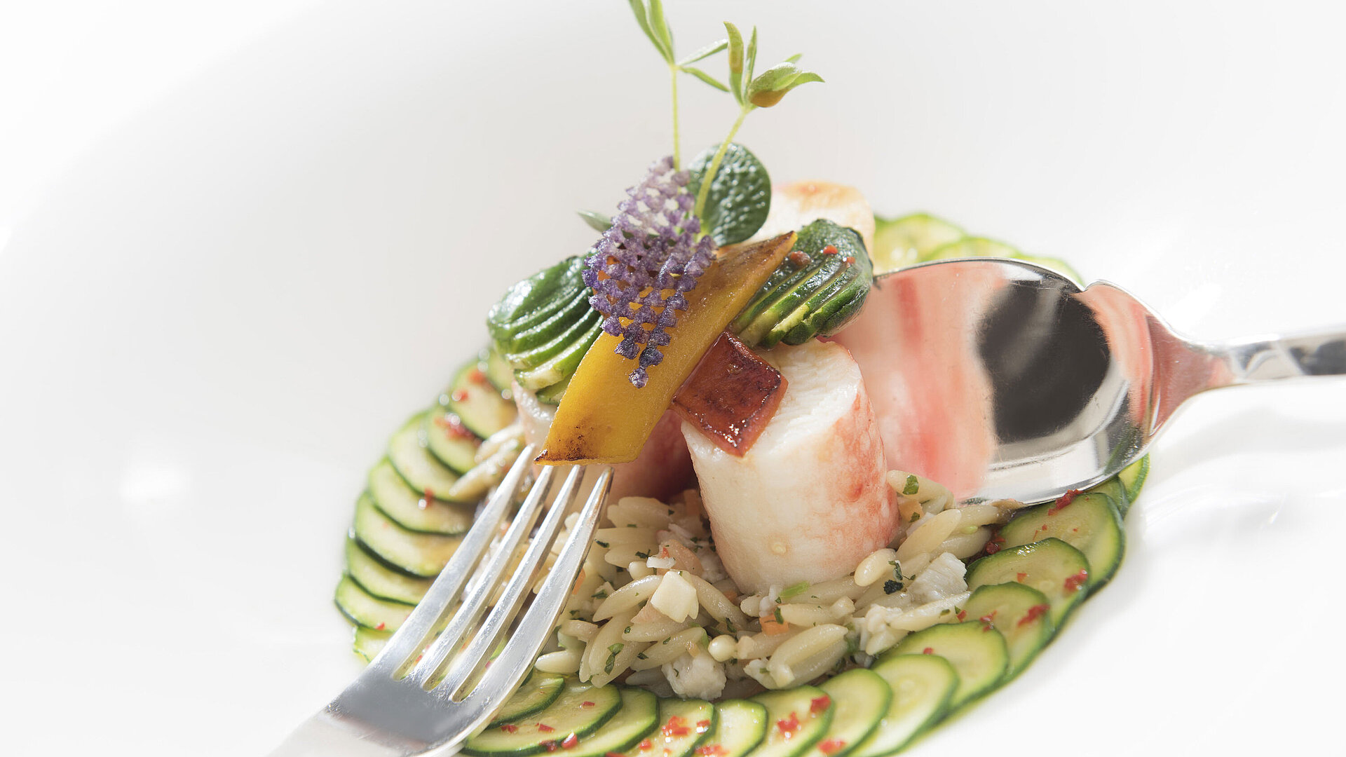 Fine gourmet dish with cucumber slices, rice, and vegetables, served with spoon and fork at the Orangerie.