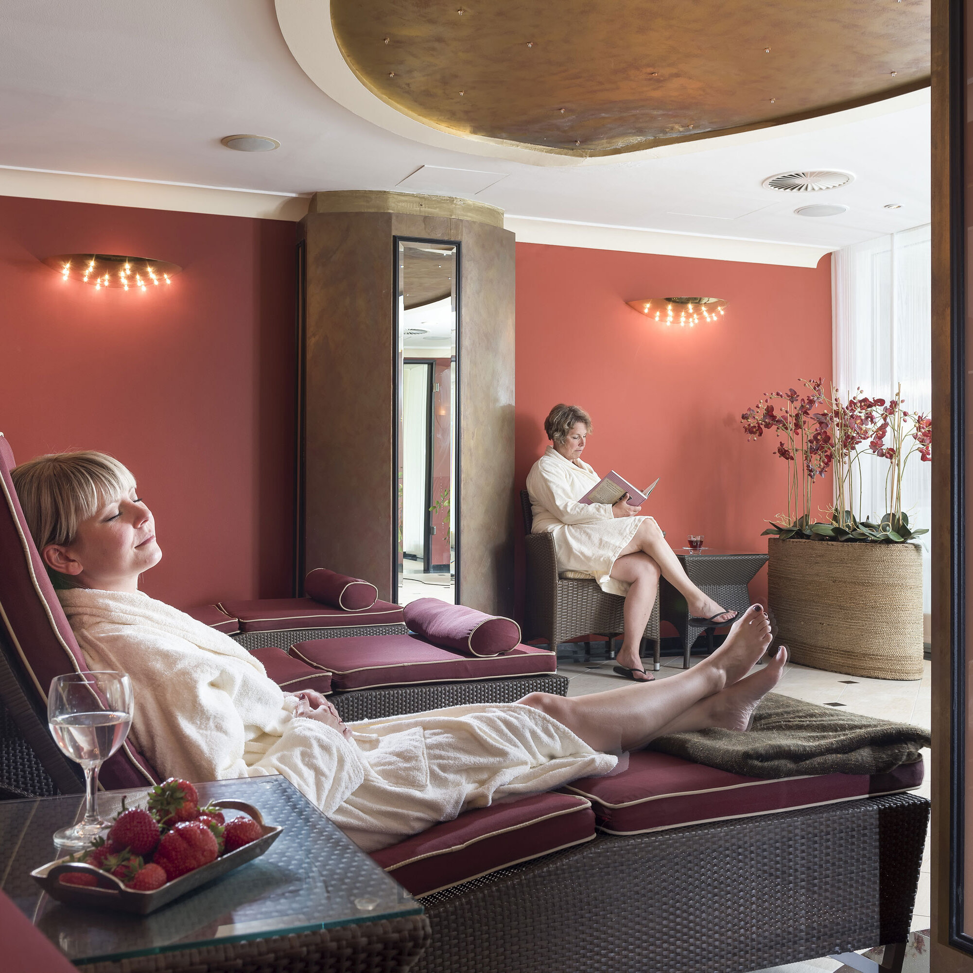 Relaxation room with red walls at Maritim Seehotel Timmendorfer Strand, guests relaxing on loungers.