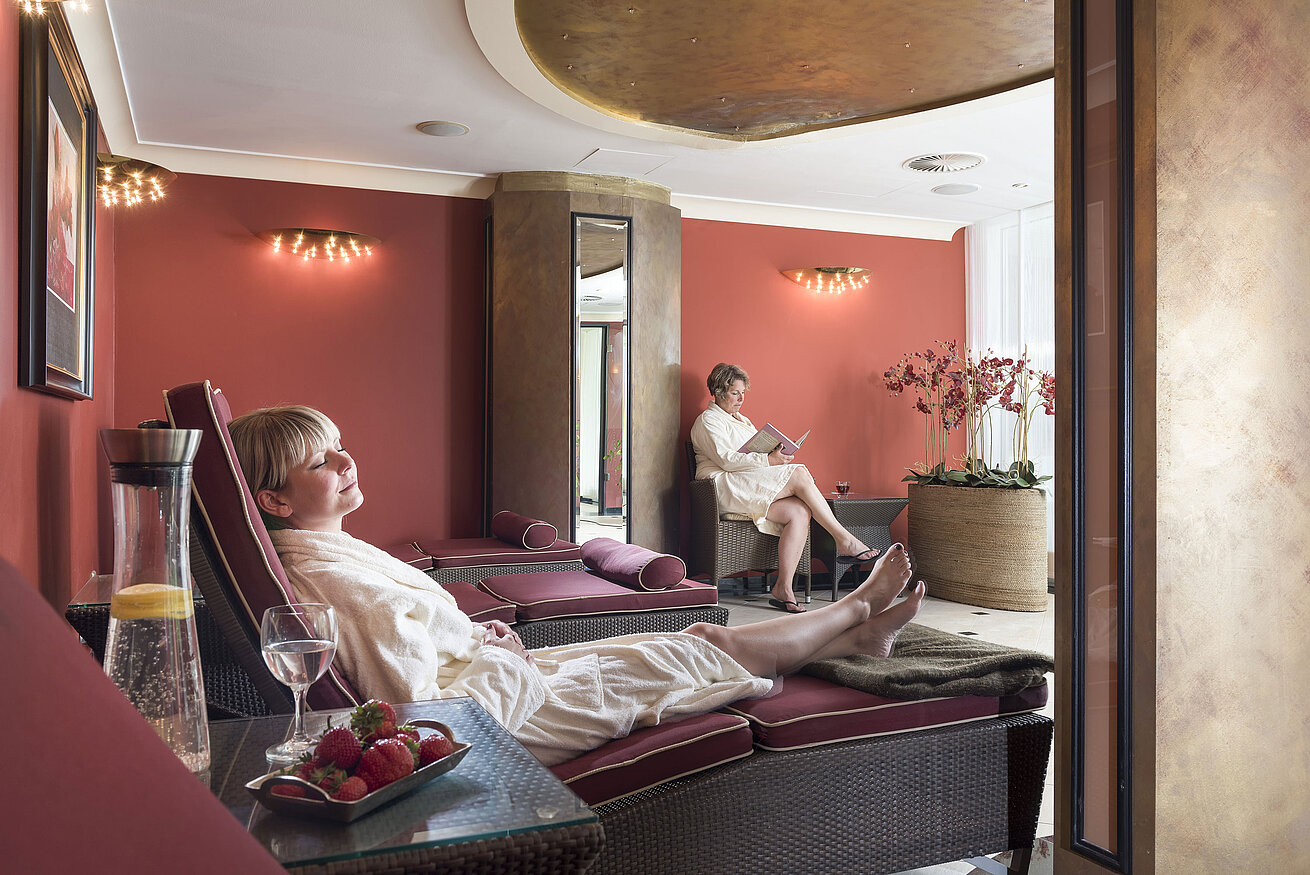 Salle de repos aux murs rouges au Maritim Seehotel Timmendorfer Strand, clients se relaxant sur des transats.