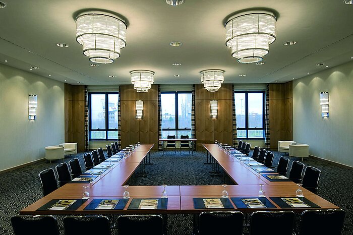 Modern conference room at Maritim Hotel Düsseldorf with U-shaped seating, large windows, and elegant lighting.
