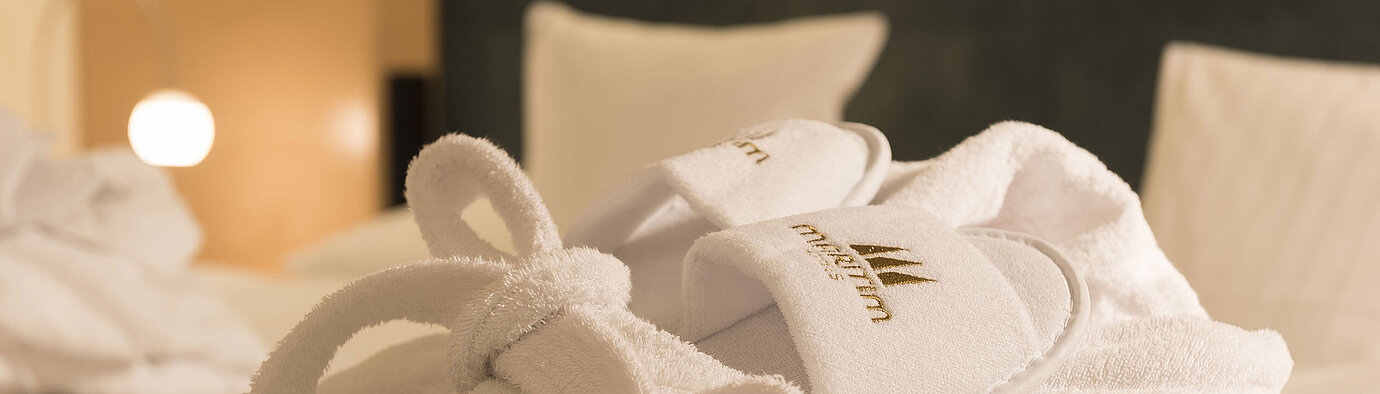 Un morbido accappatoio e pantofole con il logo Maritim su un letto al Maritim proArte Hotel Berlin.