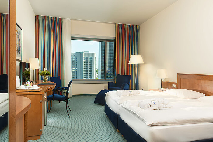 Camera superior al Maritim Hotel Frankfurt con letto matrimoniale, scrivania, area salotto e vista sulla skyline.