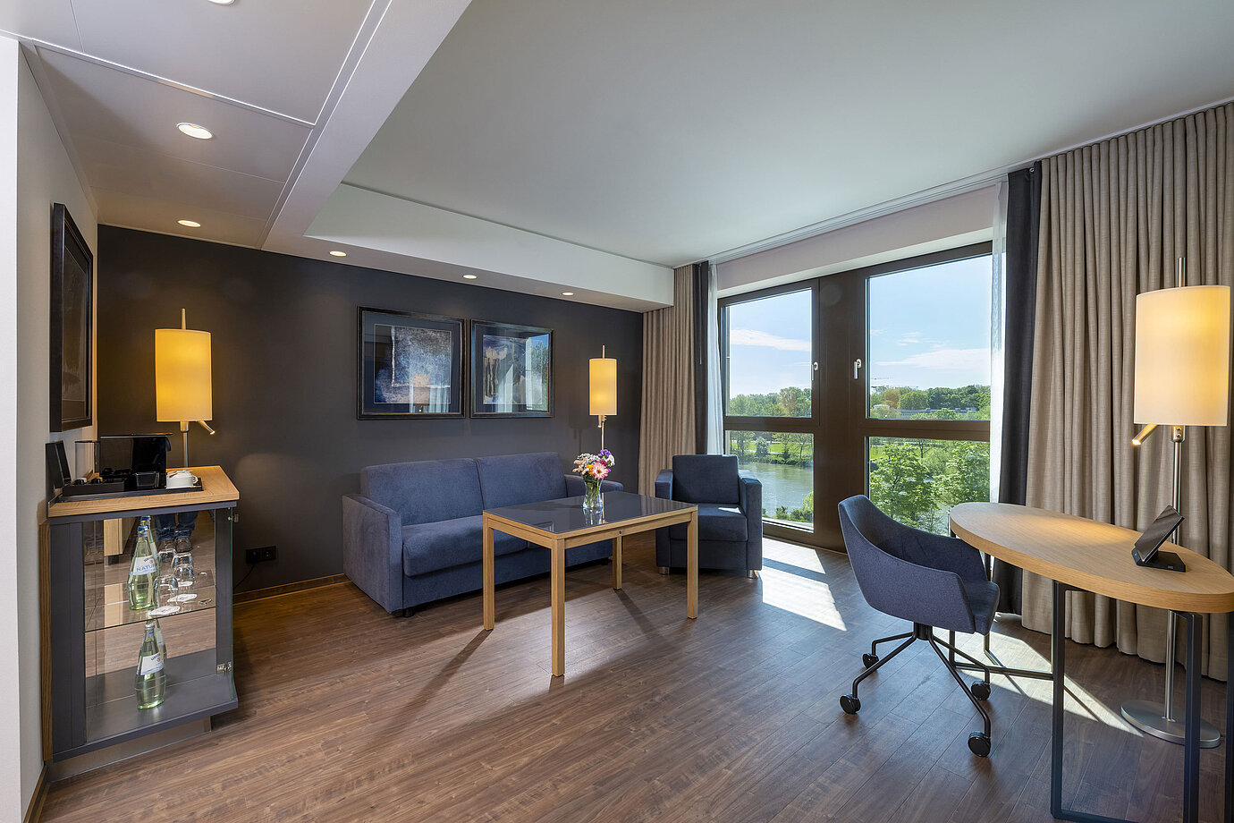 Suite luminosa con zona de estar, gran ventana y vista a la naturaleza en el Maritim Hotel Ingolstadt.