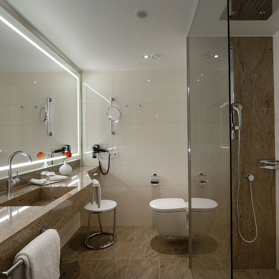 Baño en el Maritim Hotel Ingolstadt con ducha de cristal y espejo grande.