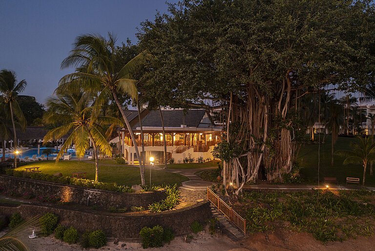 A hotel complex at night, surrounded by tropical plants and atmospheric lighting