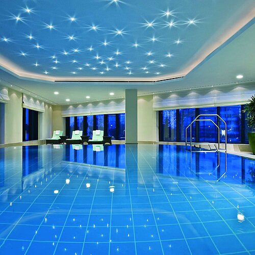 Piscina coperta illuminata al Maritim Hotel Düsseldorf con lettini moderni e finestre panoramiche.