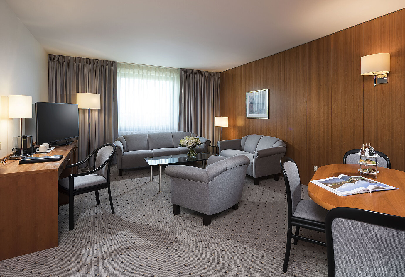 Junior Suite con soggiorno elegante, divano, poltrone, scrivania e TV al Maritim Hotel Hannover.