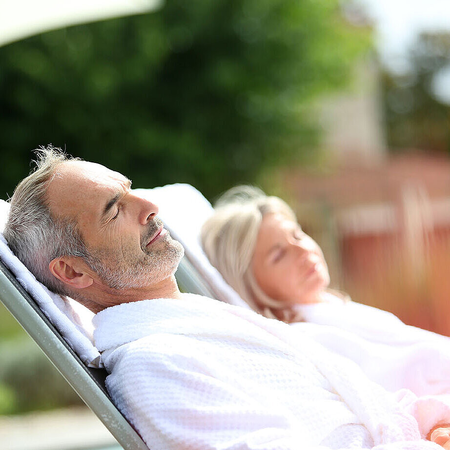 Man and woman in bathrobes relaxing on outdoor loungers and enjoying a peaceful break.