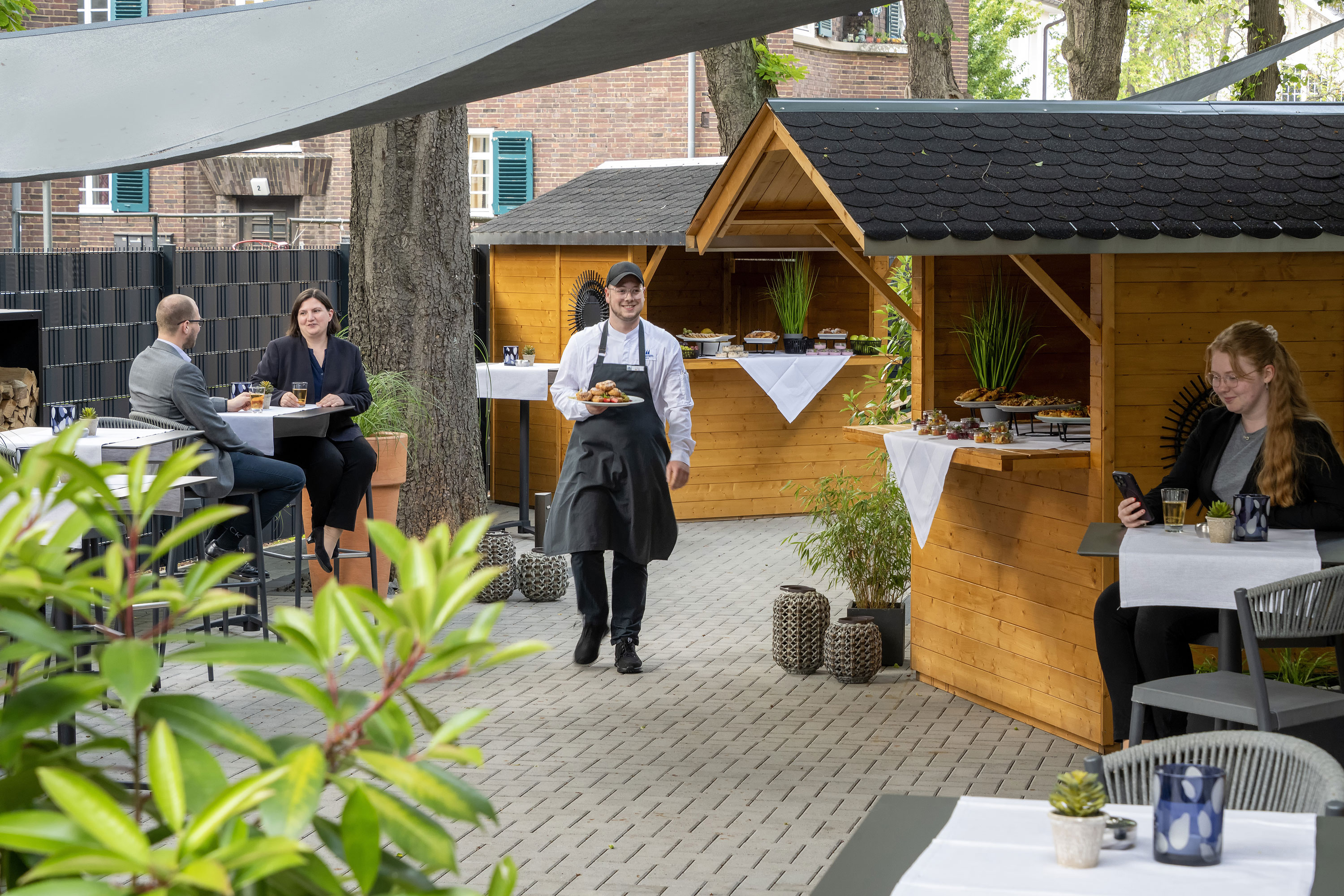 Terraza exterior Camarero sirviendo comida en un evento en la terraza del Maritim Hotel Darmstadt con cabañas de madera