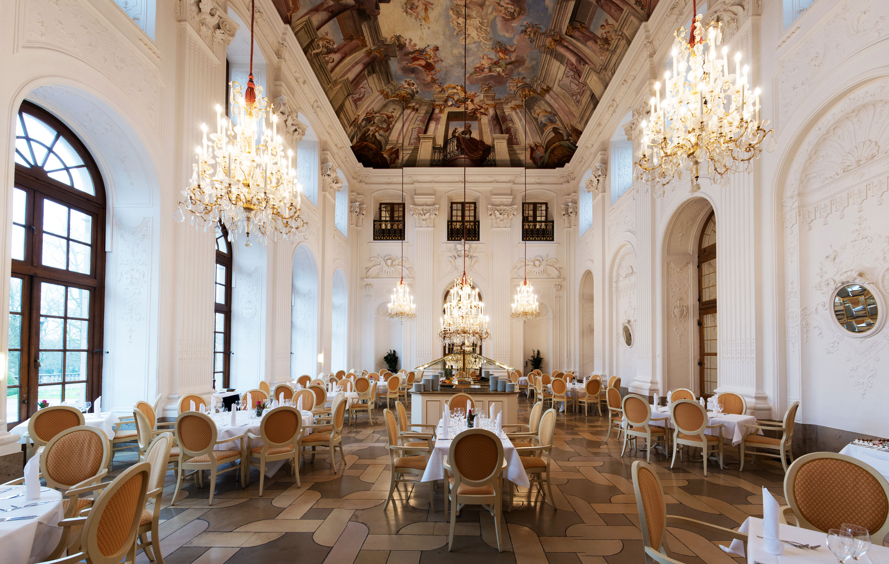 Elegant Apollo Hall at Maritim Hotel Fulda with chandeliers, fresco ceiling, and stylishly set tables.
