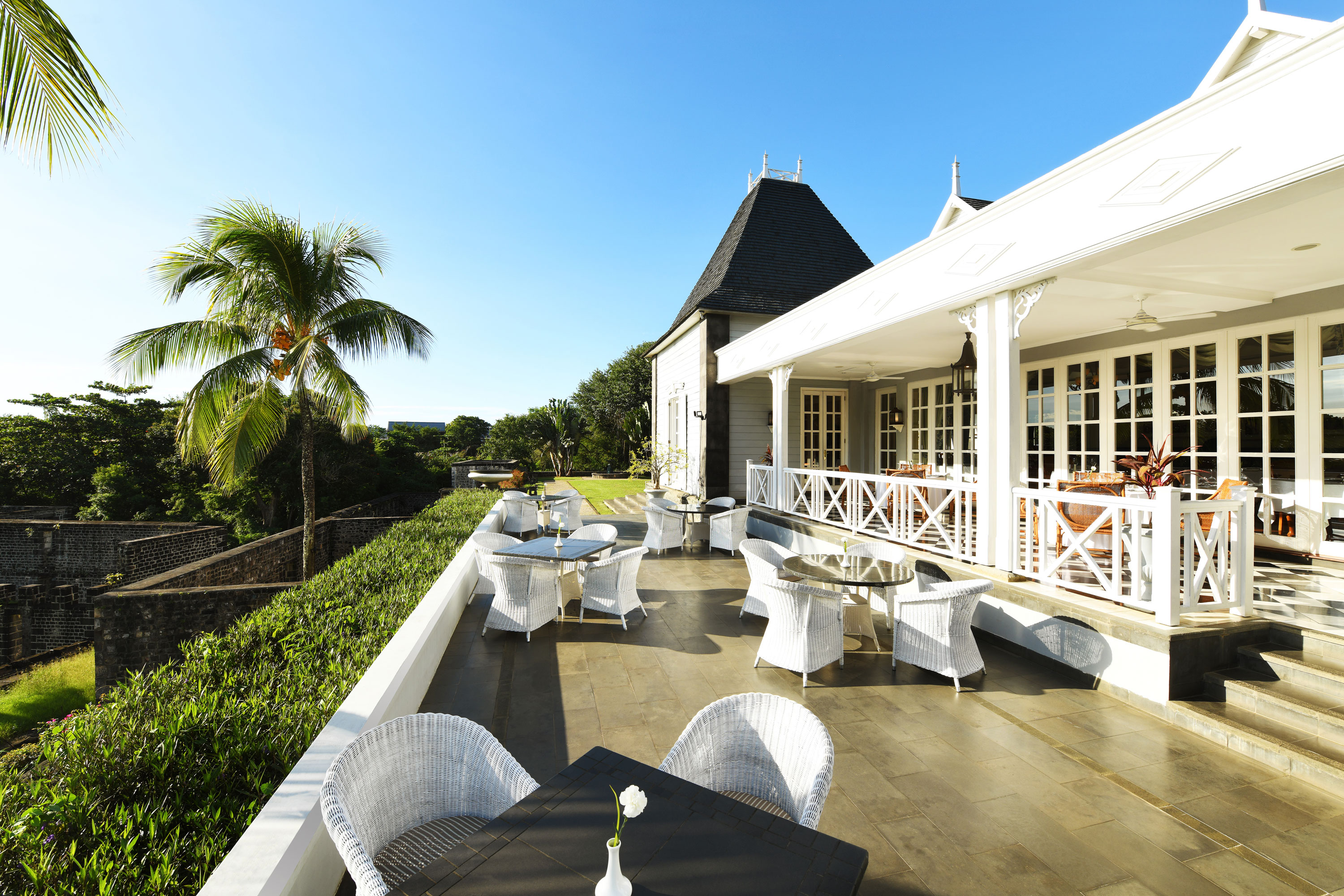 Espace événementiel "Château Mon Désir" Terrasse avec des meubles en rotin élégants, surplombant le jardin et le bâtiment en arrière-plan